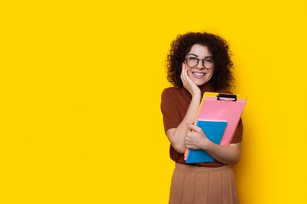 Mooie blanke student met krullend haar en bril poseren terwijl ze enkele boeken vasthoudt