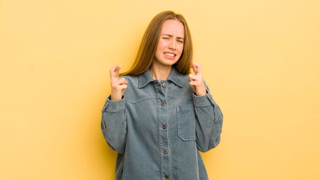 Mooie blanke vrouw die angstig vingers kruist en hoopt op veel geluk met een bezorgde blik