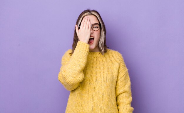 Mooie blanke vrouw die er slaperig verveeld uitziet en gaapt met hoofdpijn en een hand die de helft van het gezicht bedekt