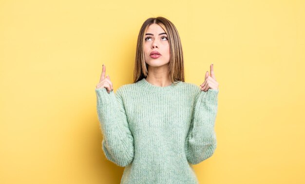 Mooie blanke vrouw die geschokt, verbaasd en met open mond kijkt, met beide handen naar boven gericht om ruimte te kopiëren