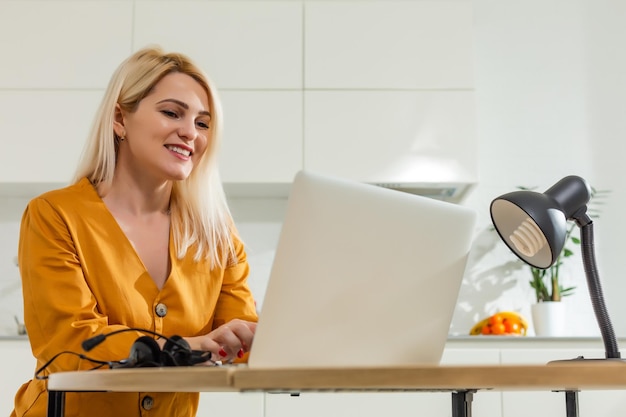 Mooie blanke vrouw die op laptop werkt. Keuken achtergrond.