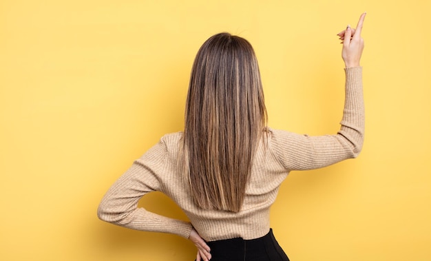 Mooie blanke vrouw die staat en wijst naar object op kopieerruimte, achteraanzicht