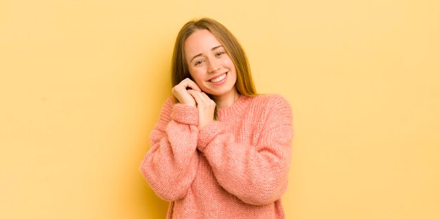 Mooie blanke vrouw die verliefd is en er schattig schattig en gelukkig uitziet, romantisch glimlachend met de handen naast het gezicht