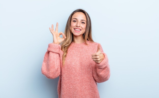 Mooie blanke vrouw die zich gelukkig, verbaasd, tevreden en verrast voelt, oke toont en duimen omhoog gebaren, glimlachend