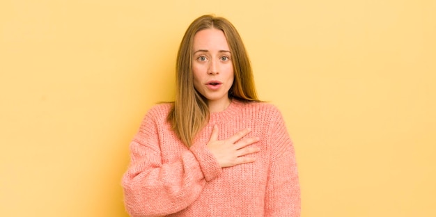 Mooie blanke vrouw die zich geschokt en verrast voelt en glimlacht en haar hand ter harte neemt, blij om degene te zijn of dankbaarheid te tonen