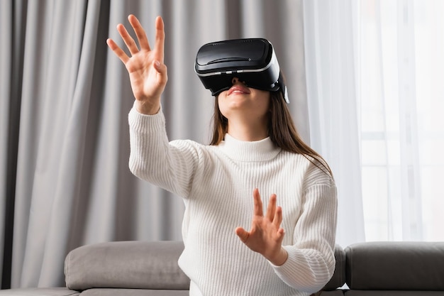 Mooie blanke vrouw gebruikt een VR-headset die een onzichtbaar scherm aanraakt terwijl ze in de woonkamer zit