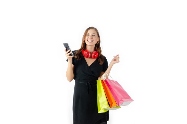 Mooie blanke vrouw in zwarte jurk met mobiele telefoon en boodschappentassen geïsoleerd op een witte achtergrond, levensstijl, slimme communicatietechnologie, online winkelen en online betalen concept