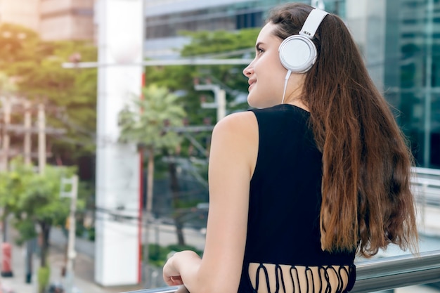 Mooie blanke vrouw luisteren muziek met koptelefoon in de stad.