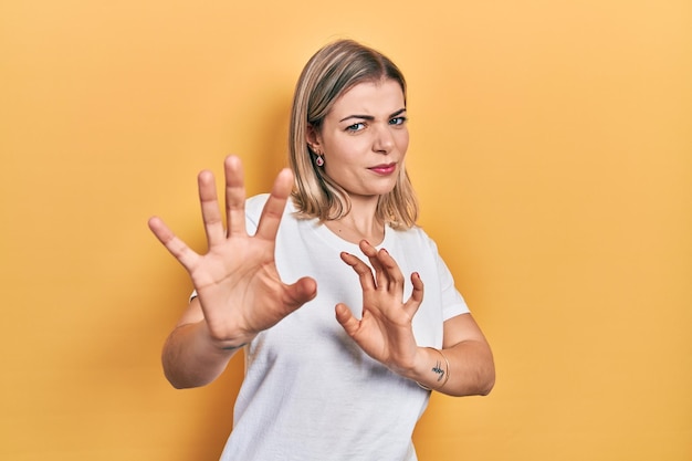 Mooie blanke vrouw met casual wit t-shirt walgende uitdrukking, ontevreden en angstig walgingsgezicht doen omdat afkeerreactie. met opgeheven handen