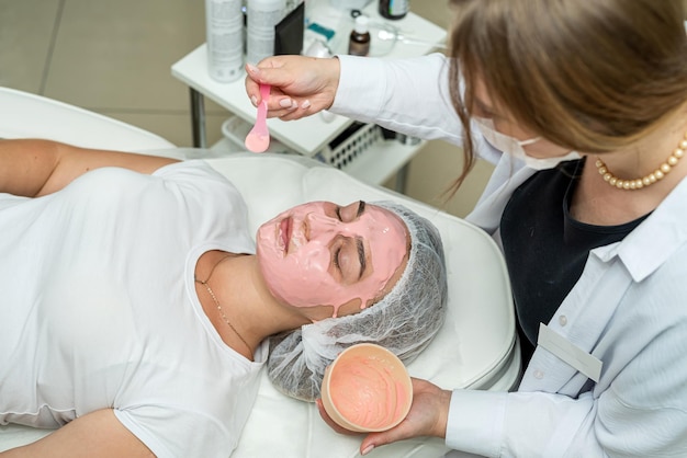 Foto mooie blanke vrouw met een roze klei gezichtsmasker in een schoonheidssalon