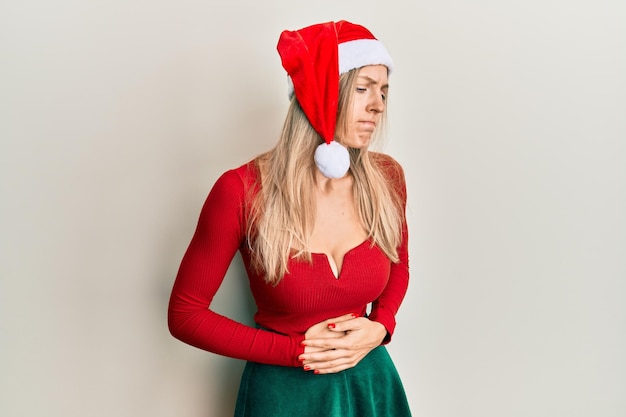 Mooie blanke vrouw met kerstkostuum en hoed met de hand op de buik omdat indigestie pijnlijke ziekte ongemak pijn concept