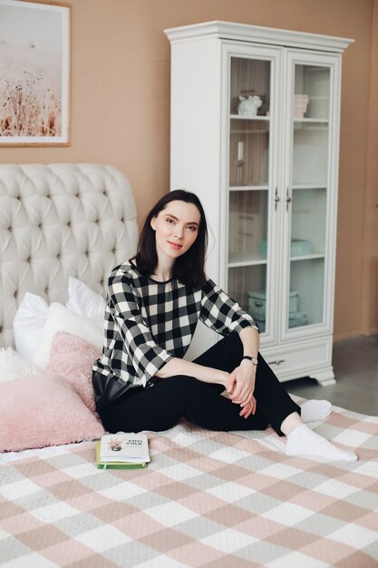 Mooie blanke vrouw met kort donker haar in een gezellige trui houdt een boek vast en glimlacht