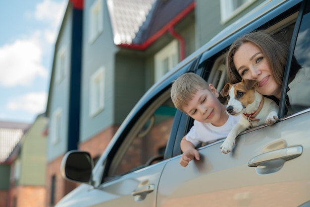 Mooie blanke vrouw reist met een kind en een hond Moeder en zoon leunden uit het autoraam in een omhelzing met een puppy van Jack Russell Terrier Gelukkige familie gaat op autorit