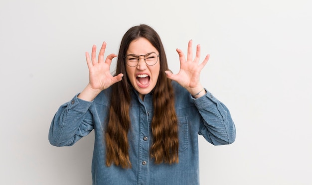 Mooie blanke vrouw schreeuwend in paniek of woede geschokt doodsbang of woedend met handen naast hoofd