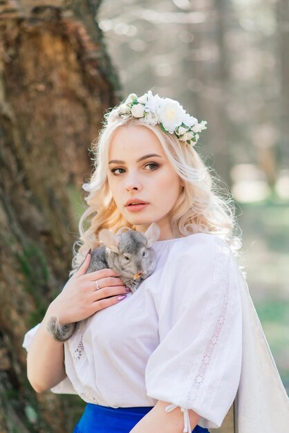 Mooie blauwe en blonde ongebruikelijke langharige vrouw in een lange jurk houdt een chinchilla vast