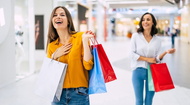 Mooie blije en opgewonden jonge vriendinnen met papieren zakken lopen rond in het winkelcentrum