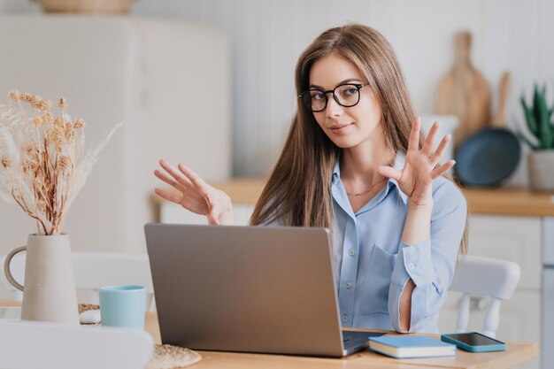 Mooie blonde blanke vrouw in blauw shirt en bril zit aan tafel met
