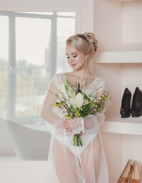 Mooie blonde bruid met een boeket bloemen in een luxe appartement. ochtend van de bruid