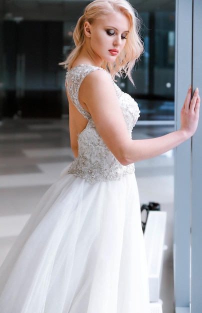 Mooie blonde bruid met kort haar en in een witte gezwollen jurk poseren voor de camera