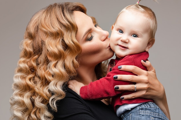 Mooie blonde dame die haar glimlachend kind vasthoudt en zachtjes zijn wang kust