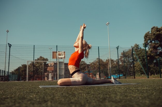 Foto mooie blonde doet stretching op het gazon van een voetbalveld