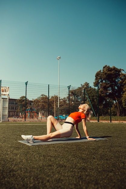 Mooie blonde doet stretching op het gazon van een voetbalveld