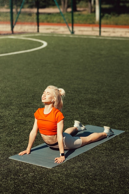 Mooie blonde doet stretching op het gazon van een voetbalveld