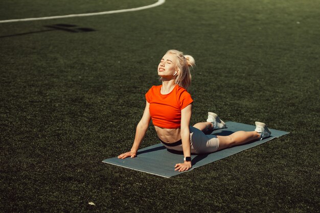 Mooie blonde doet stretching op het gazon van een voetbalveld