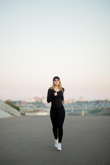 Mooie blonde fitness vrouw die buiten op de achtergrond van de stad loopt