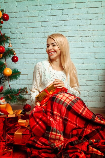 Mooie blonde gewikkelde plaid met een stel kerstcadeautjes glimlachend. Nieuwjaar. Kerststemming.