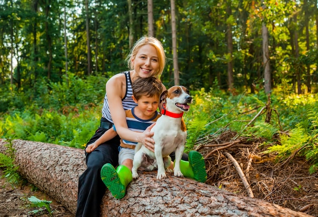 Mooie blonde haarmoeder zit op een boomstam met zoon en een hond in het bos