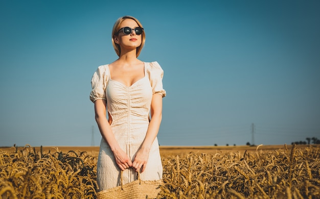 Mooie blonde haarvrouw in witte jurk in tarweveld met blauwe lucht