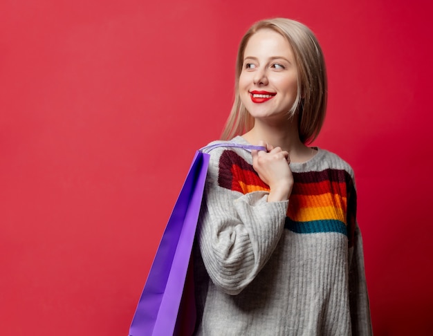 Mooie blonde in trui met boodschappentassen op rood