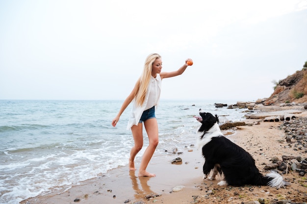 Mooie blonde jonge vrouw spelen met hond op het strand