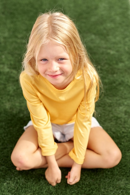 Foto mooie blonde meisje gele t-shirt zittend op groen gras top view