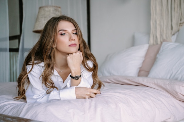 Mooie blonde meisje, zittend op het bed in de slaapkamer