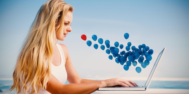 Mooie blonde met behulp van haar laptop op het strand tegen rode en blauwe ballonnen