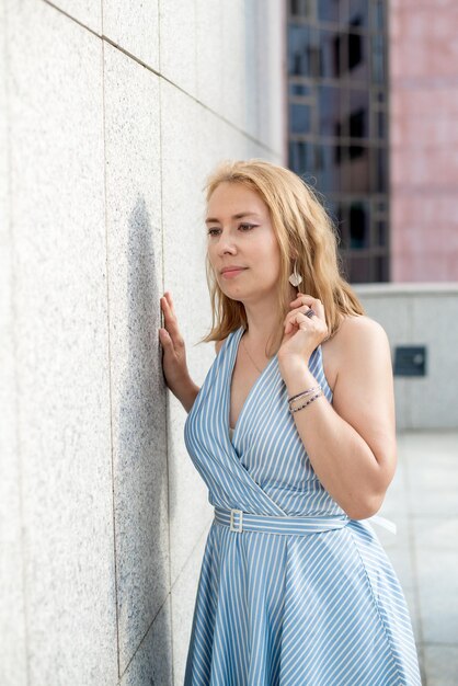 Mooie blonde poseren in een blauwe jurk op straat