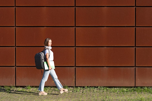 Mooie blonde student die op een zonnige dag langs een stadsmuur loopt