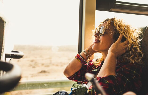 Mooie blonde volwassen vrouw die geniet van het reizen in de bus of trein die muziek luistert met een koptelefoon