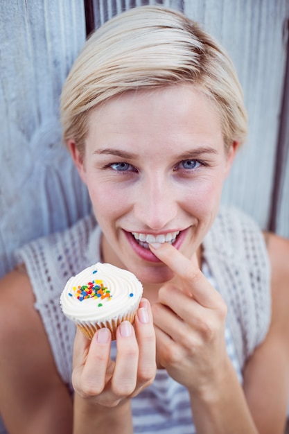 Mooie blonde vrouw die de cupcake proeft