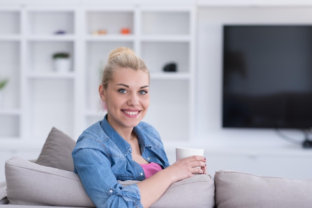 mooie blonde vrouw die geniet van een kopje koffie zittend op een bank in haar appartement