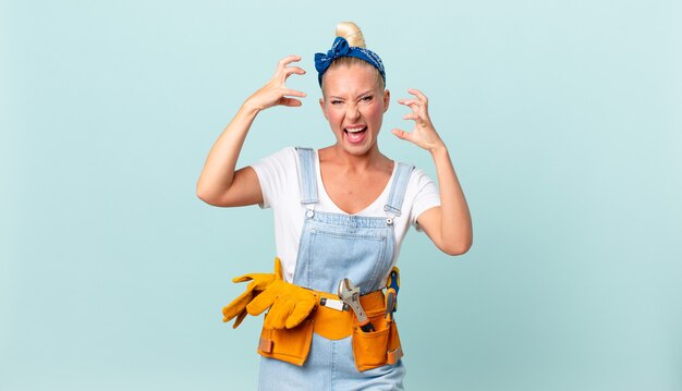 mooie blonde vrouw die met handen in de lucht schreeuwt en huisconcept repareert