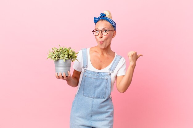 mooie blonde vrouw die verbaasd kijkt in ongeloof en een plant vasthoudt