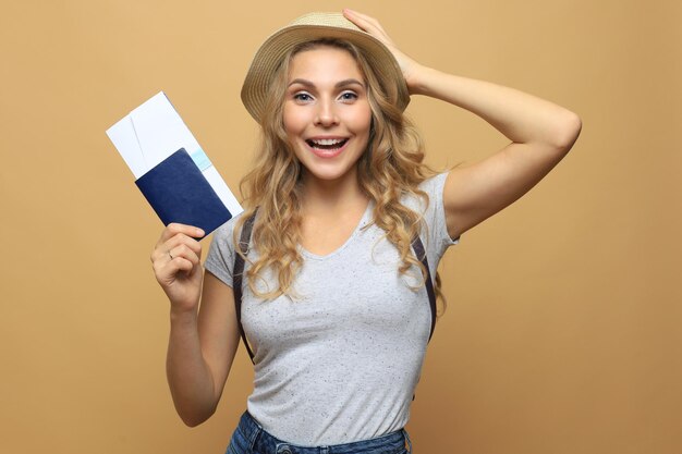 Mooie blonde vrouw die zomerkleren draagt die met paspoort met kaartjes over beige achtergrond stellen.