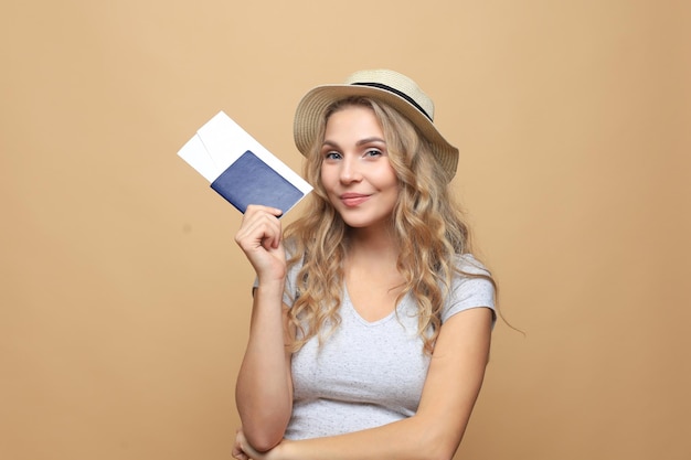 Mooie blonde vrouw die zomerkleren draagt die met paspoort met kaartjes over beige achtergrond stellen.