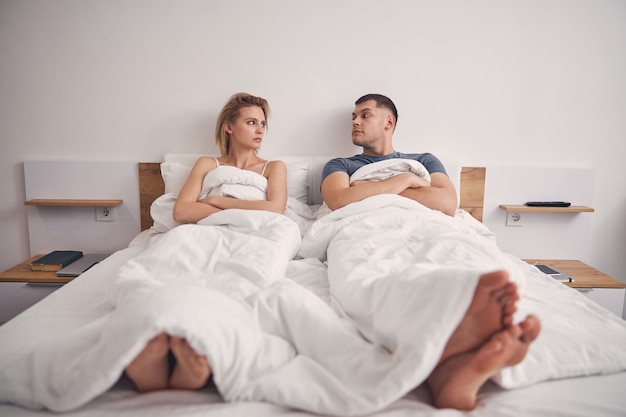 Mooie blonde vrouw en brunette man kijken boos terwijl ze in bed liggen