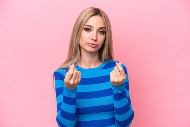 Mooie blonde vrouw geïsoleerd op roze achtergrond geld verdienen gebaar maar is geruïneerd