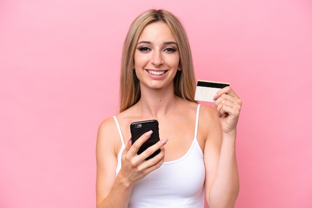 Mooie blonde vrouw geïsoleerd op roze achtergrond kopen met de mobiel met een creditcard