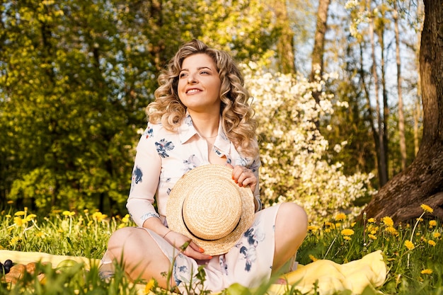 Mooie blonde vrouw - gelukkige levensstijl, weekendje uit voor een wandeling in een picknickpark in de zomertuin, model zit op plaid met eten - zomerweer